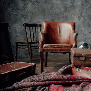 A vintage leather armchair and a classic wooden chair in a rustic setting, showcasing the timeless appeal of antique furniture upholstery. Image titled 'The History of Upholstery' highlights traditional craftsmanship and restoration services for unique pieces.