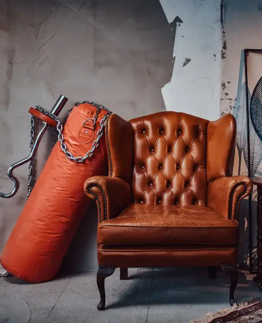 A vintage-style brown leather armchair with tufted leather upholstery, placed in a rustic industrial setting. Ideal for showcasing timeless furniture upholstery and elegant design for homes or offices in Bahrain.